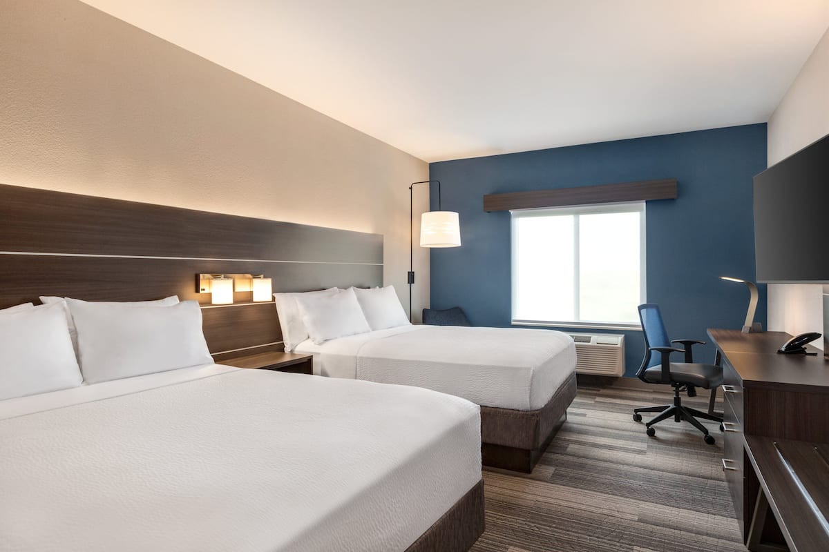 A hotel room with two beds, a desk, a chair, and a large window.