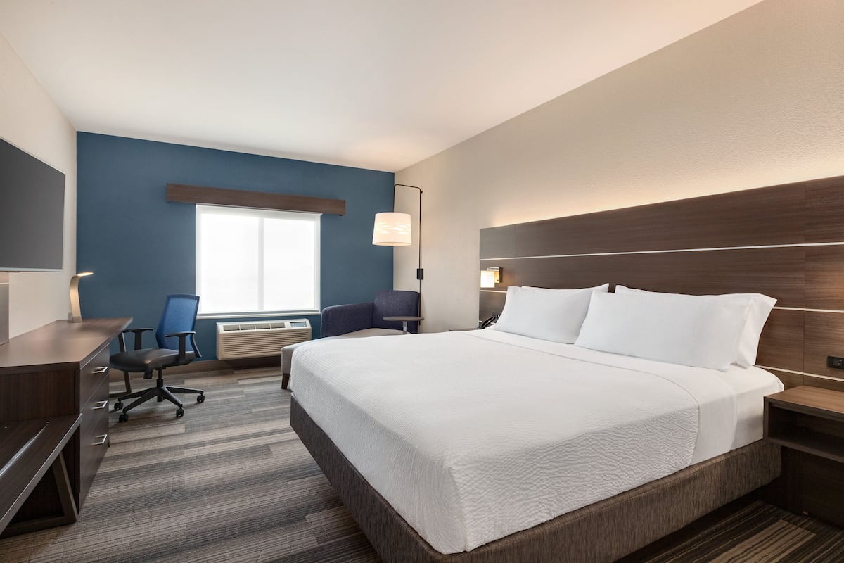 A hotel room with a large bed, a desk, a chair, and a window with blinds.