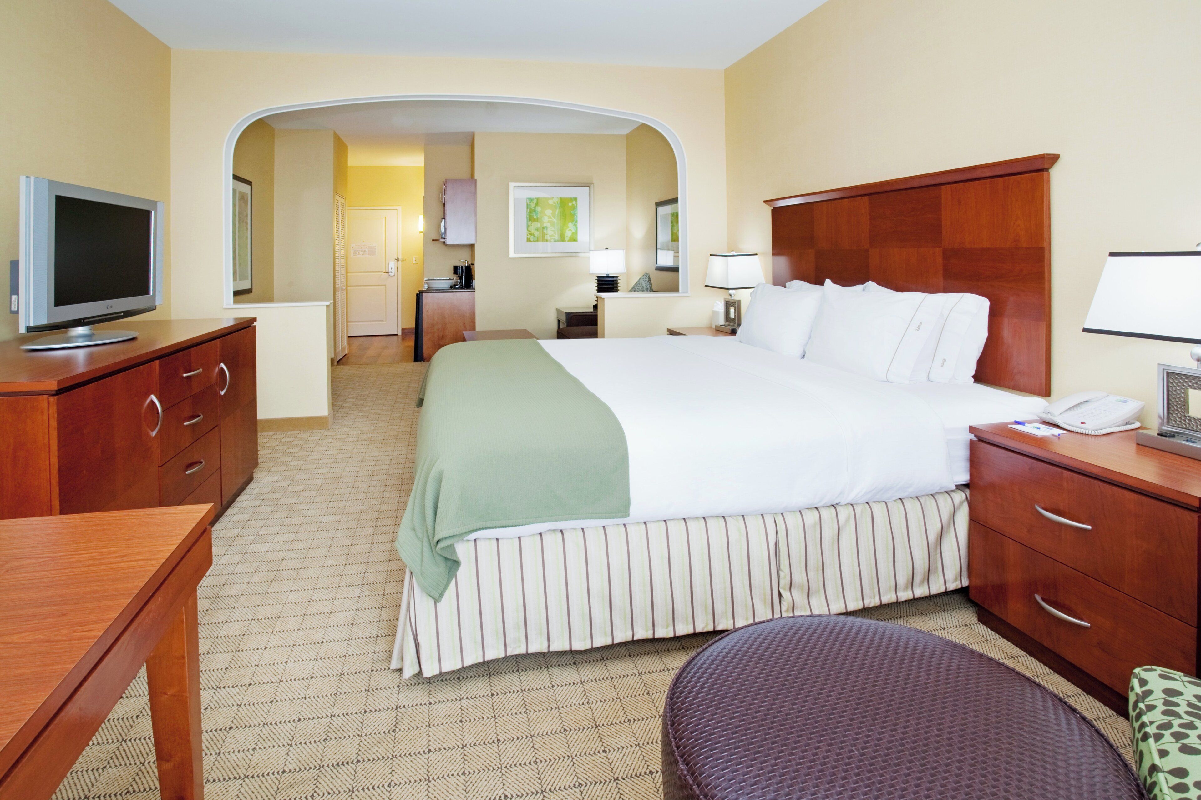 A hotel room with a bed, a desk, a television, a bathroom, and a kitchen area.