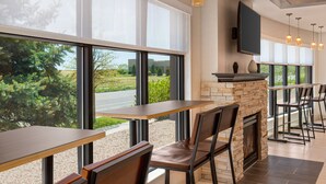 Un comedor moderno con ventanas amplias, una chimenea de piedra y varias mesas y sillas.
