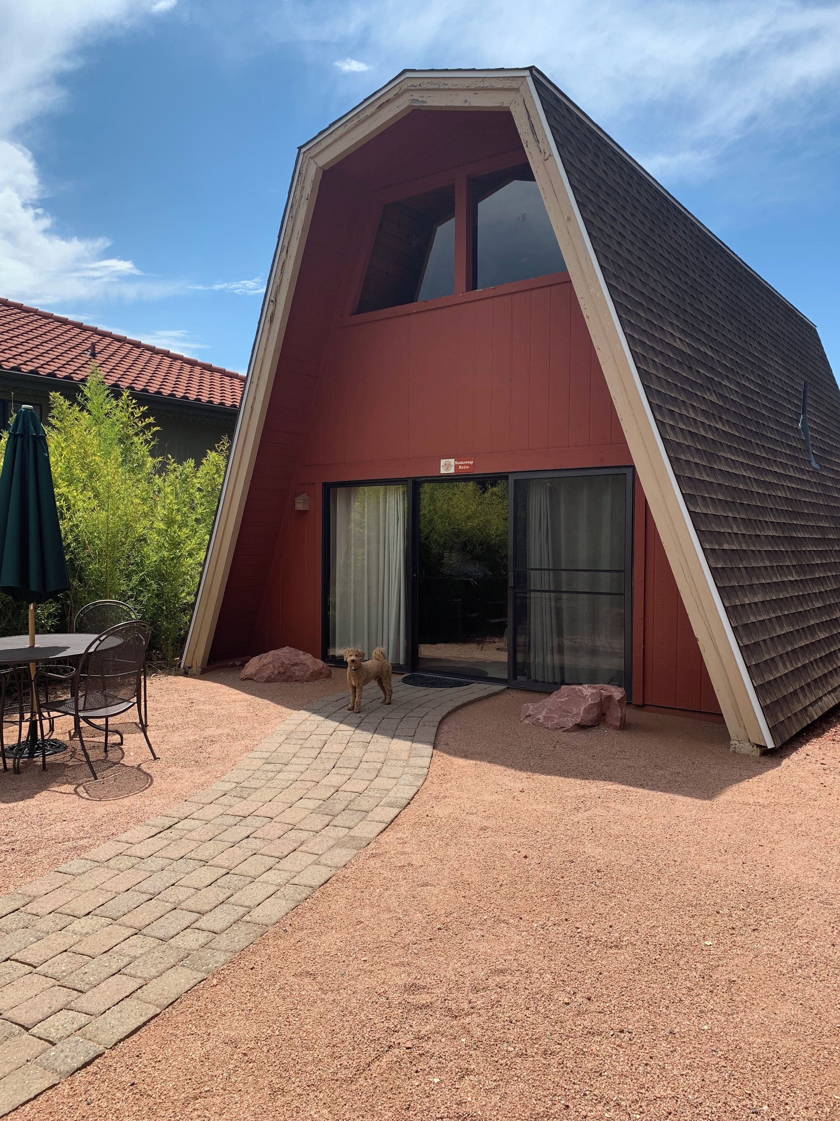 Un edificio moderno con techo inclinado, vestíbulo cubierto y patio pavimentado con mesa y sillas.