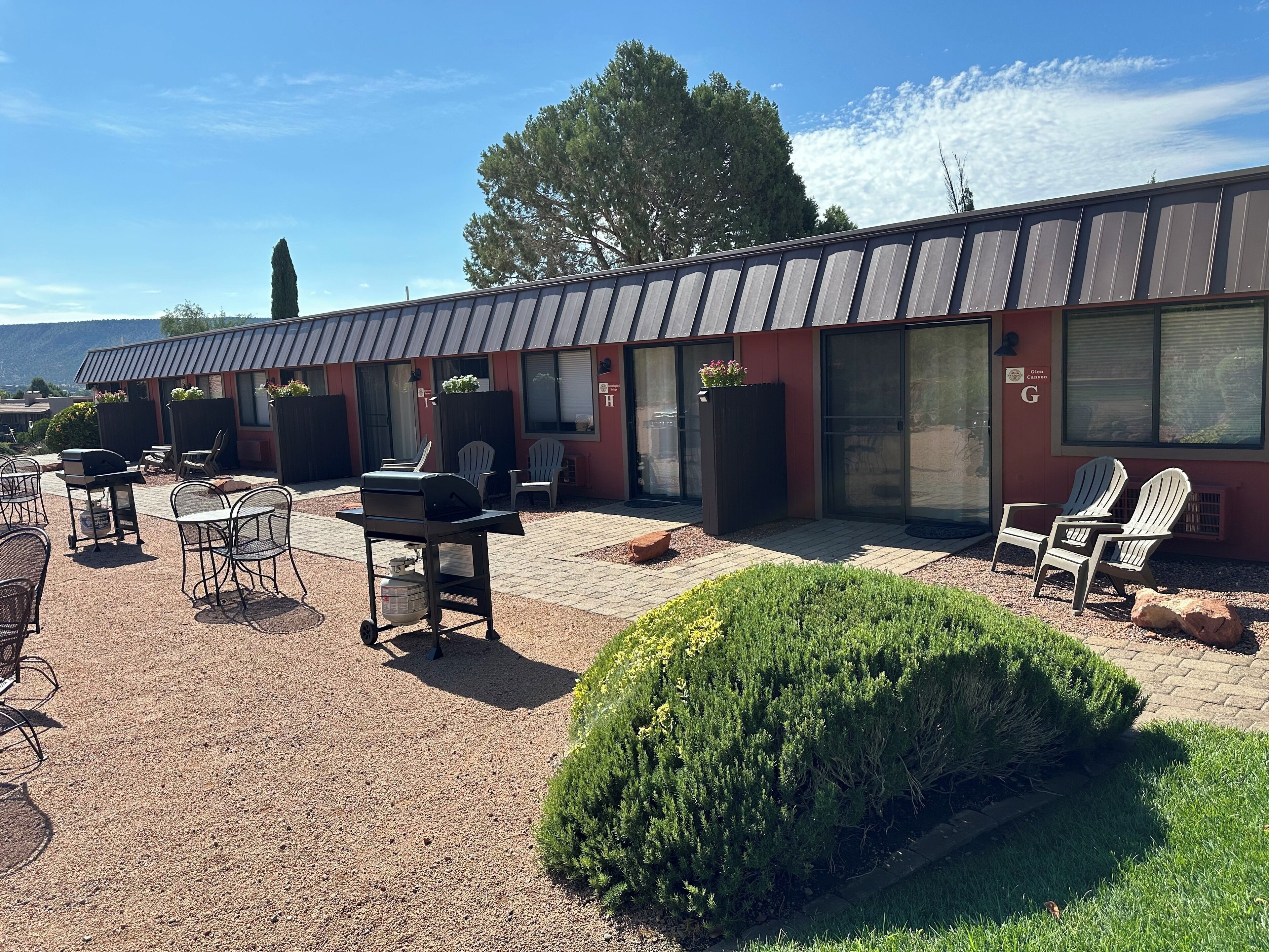 Un patio con mobiliario exterior, una parrilla y un edificio con fachada roja y techo de metal.
