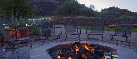 An outdoor seating area with a fire pit, chairs, and two glasses of wine.