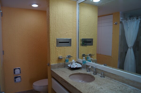 A bathroom with a beige sink, mirror, and toilet. There are toiletries on the sink counter. - Solymar Hotel (Cancun)