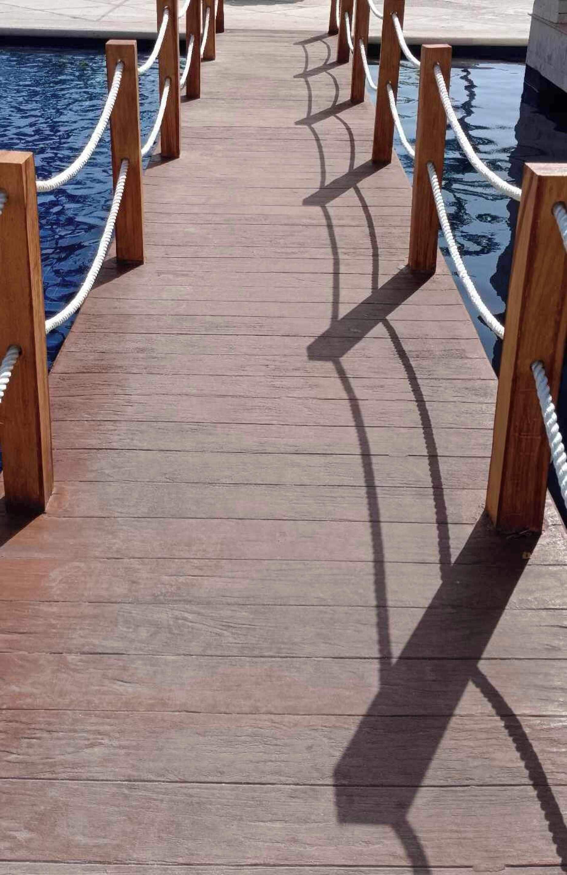A wooden deck with a rope barrier leading to a pool.