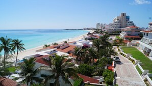 Un hotel frente al mar, con vista a la playa, palmeras y cielo despejado.