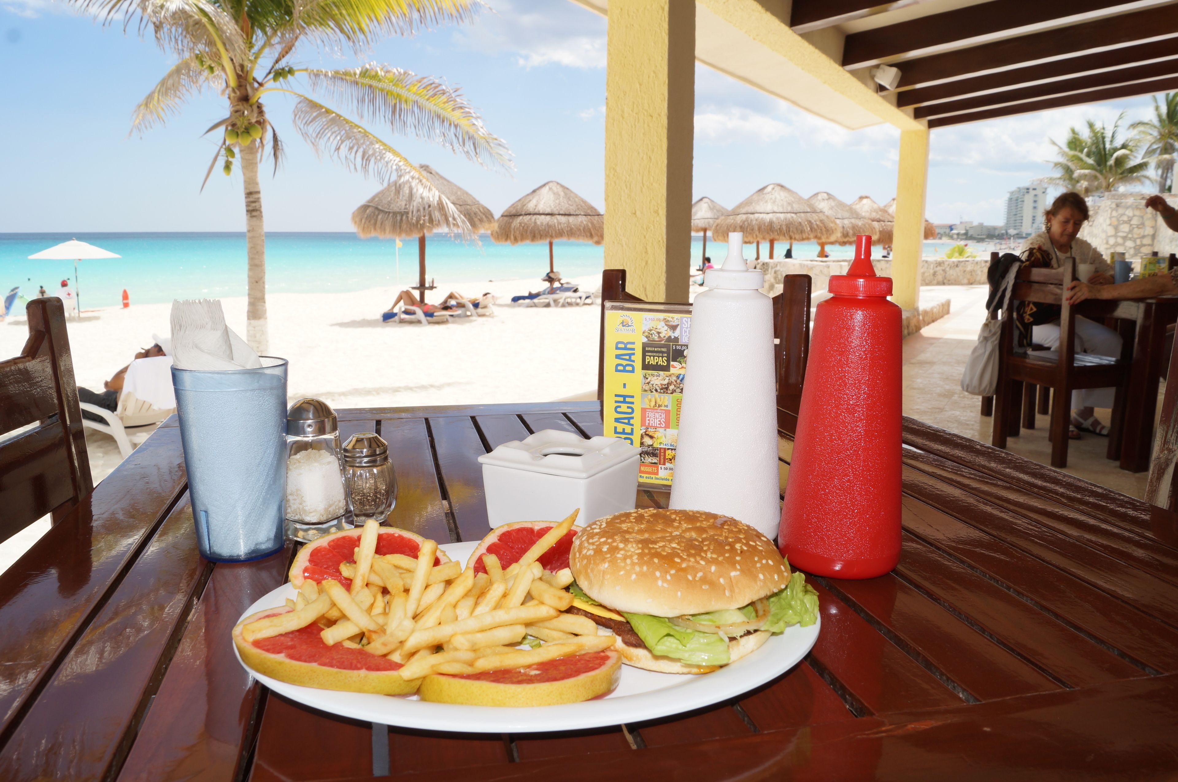 Ein Esstisch am Strand mit Mahlzeit, Strandstühlen und Blick aufs Meer.