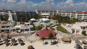 Un resort con varias construcciones, un área de piscina y una playa con tumbonas y sombrillas.