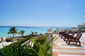 A terrace with stone railings, palm trees, and lounge chairs overlooking a beach.
