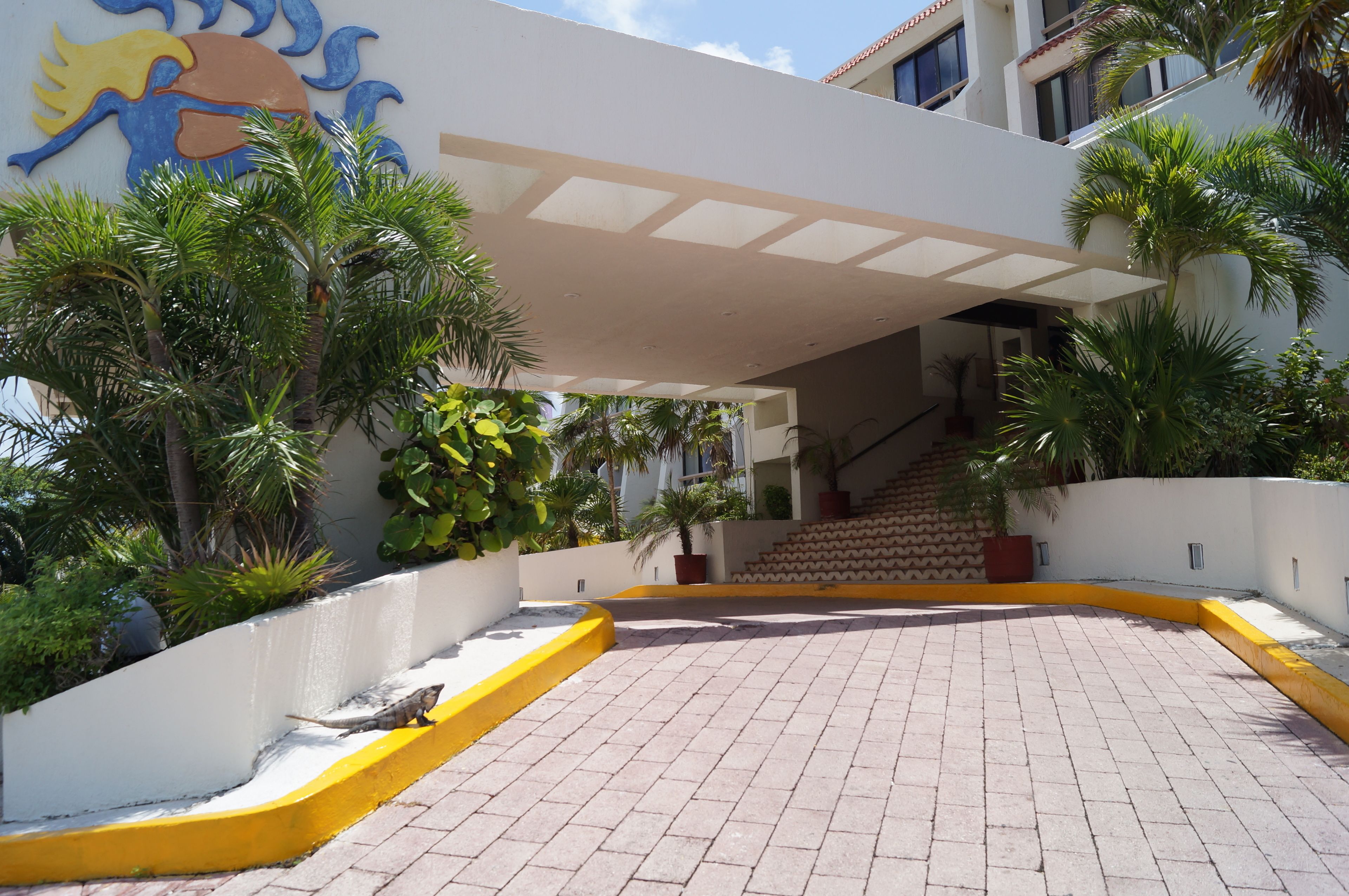 A paved courtyard with a staircase leading to an upper level, surrounded by palm trees and a decorative wall with a sun and moon motif.