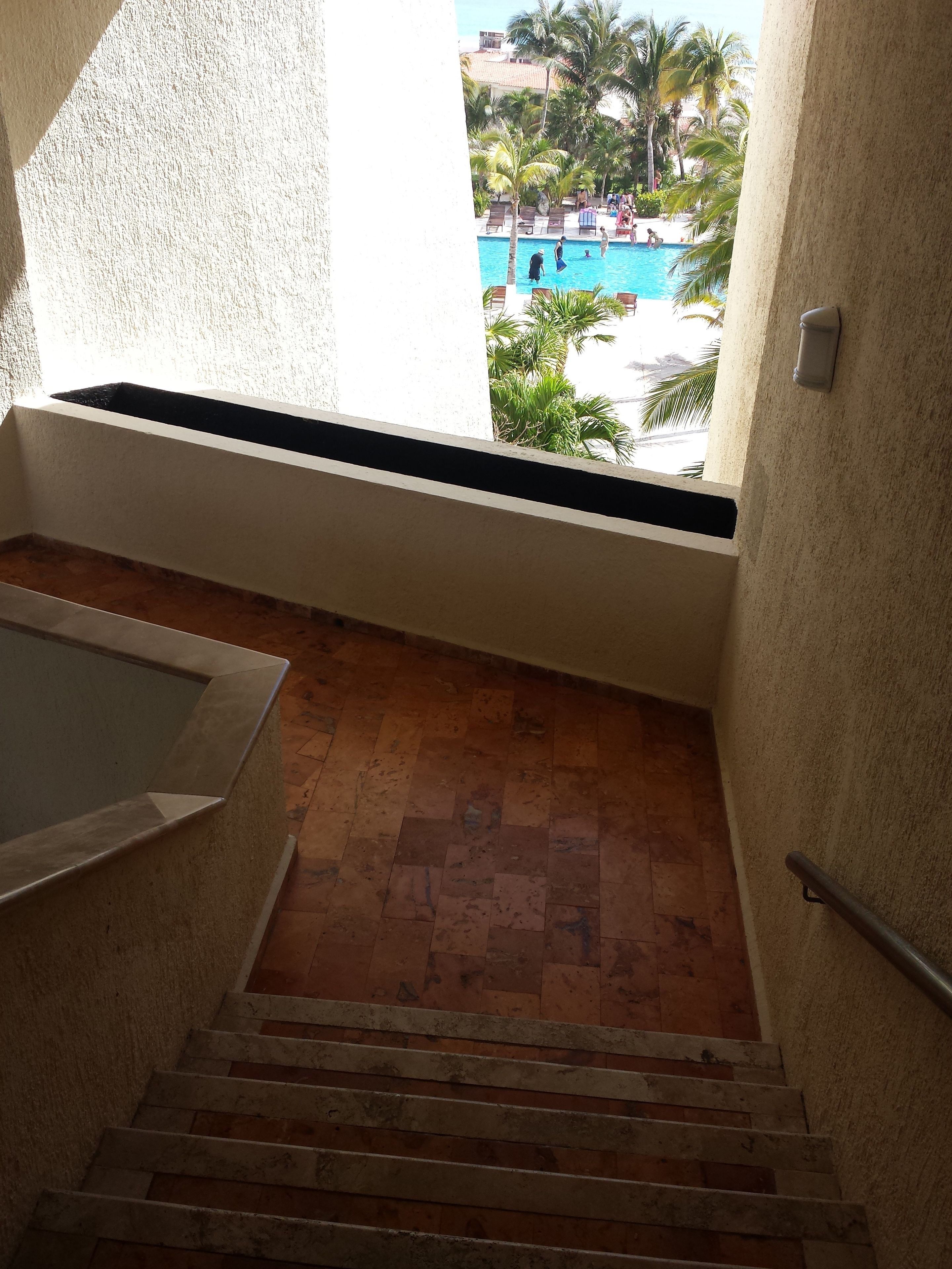 Una escalera conduce a una zona de piscina con vistas a palmeras y un cielo despejado.