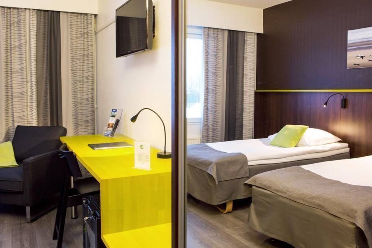 A hotel room with a desk, two beds, a TV, and curtains.