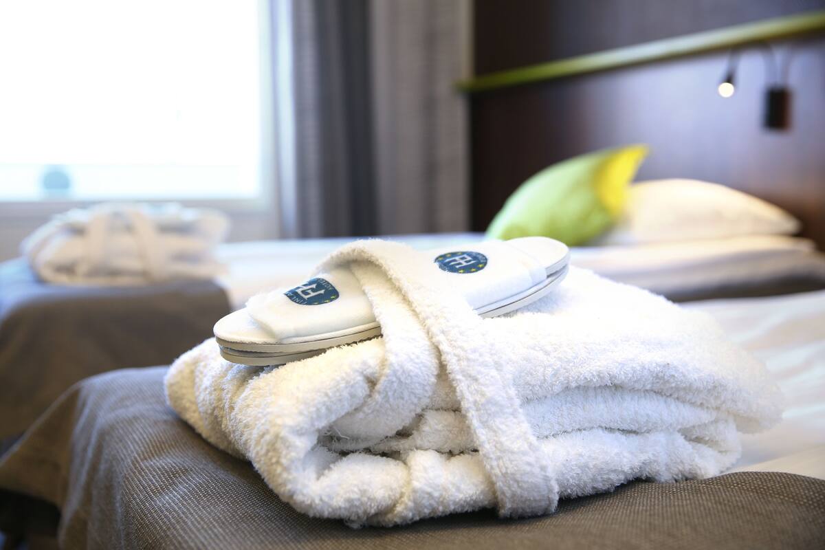 A neatly folded white towel with a logo on a bed in a hotel room.