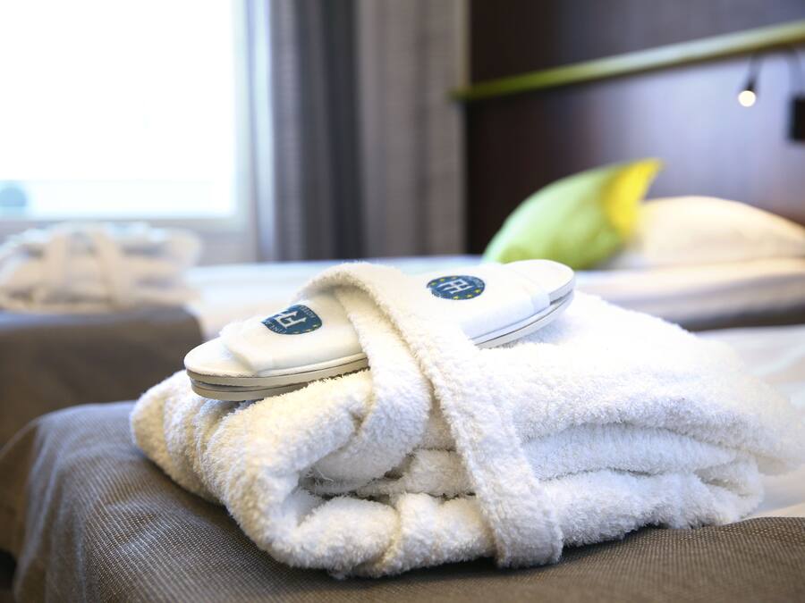 A neatly folded white towel with a logo on a bed in a hotel room.