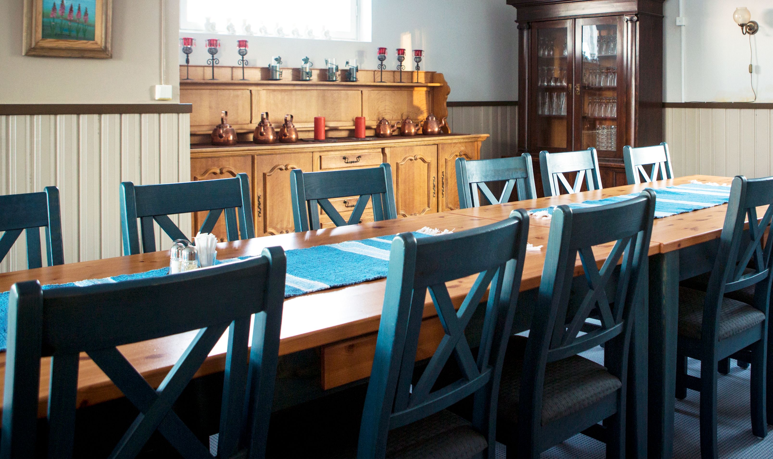 Une salle à manger avec une longue table en bois, des chaises bleues et un buffet en bois doté de portes en verre.