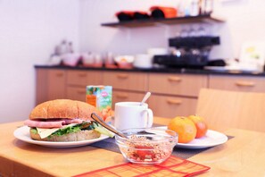 Frühstückstisch mit Sandwich, Orange und Schüssel mit Frühstückscerealien.
