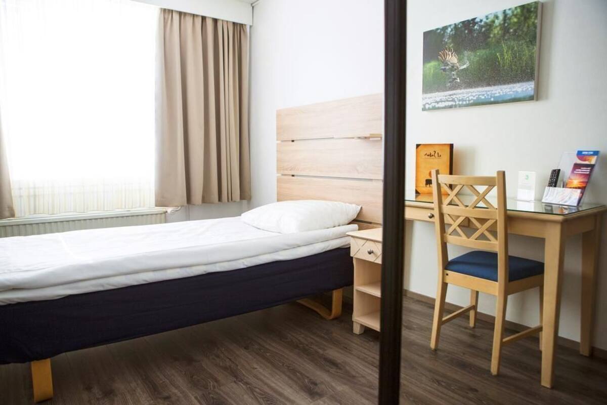 A hotel room with a bed, a desk, a chair, and a window with curtains.