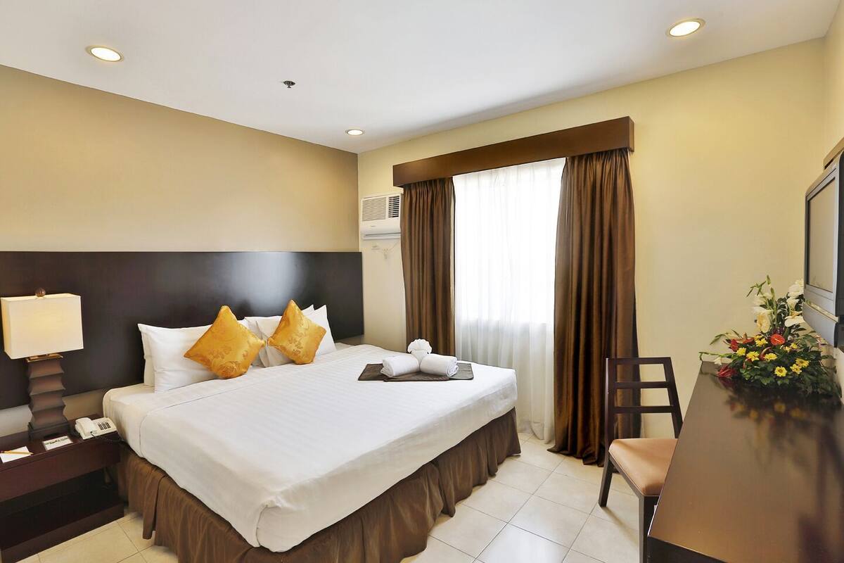 Una habitación de hotel con cama, mesita de noche, lámpara y un escritorio con silla.