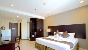 A hotel room with a bed, a desk, a chair, a wardrobe, and a bathroom. - Alpa City Suites (Mandaue)