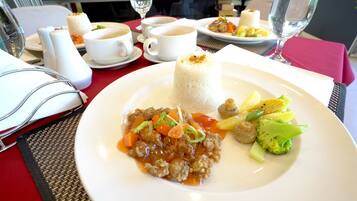 A dining table with a plate of food, including rice, meat, and vegetables, and two cups of coffee.