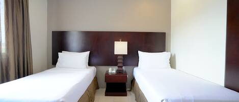 Une chambre d’hôtel avec deux lits simples, une table de chevet avec une lampe et un téléphone.
