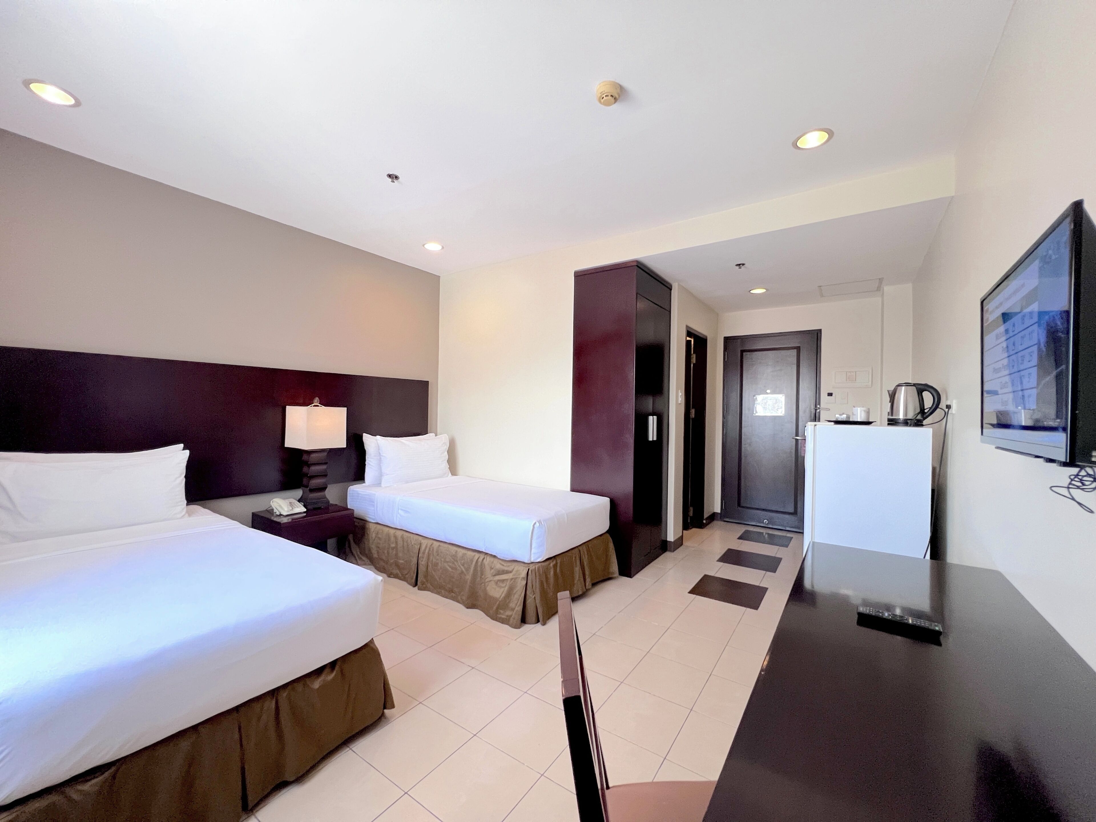 A hotel room with two beds, a desk, a television, and a door leading to a bathroom.