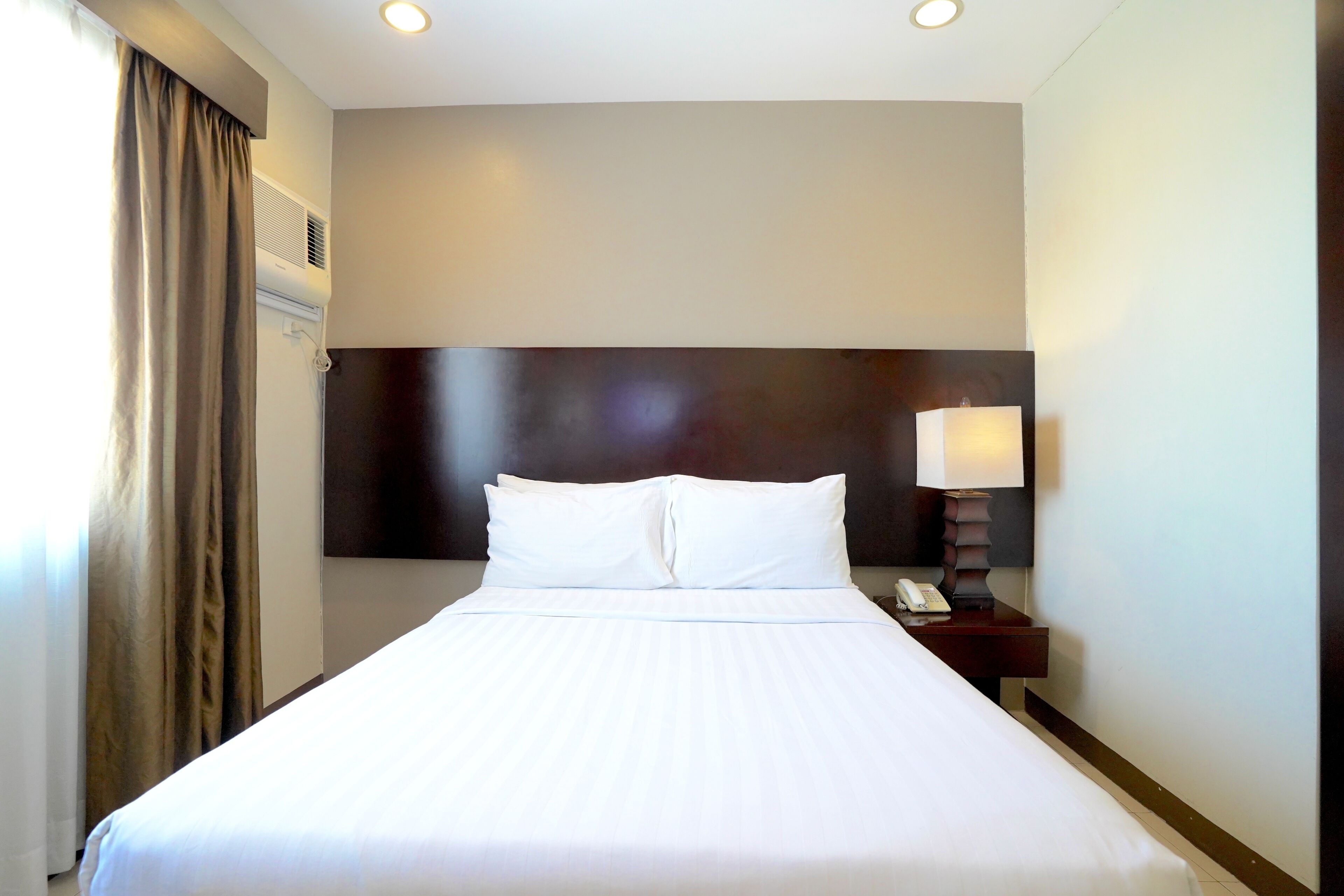 Habitación de hotel con una cama grande, una mesita de noche con lámpara y un aire acondicionado de pared.