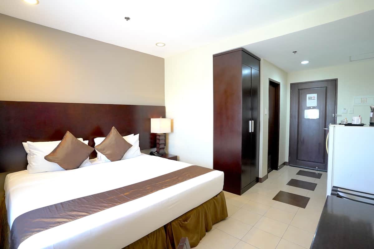 Habitación de hotel con una cama grande, un escritorio, un refrigerador y una puerta con un letrero de 'NO ENTRAR'.