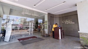 A hotel entrance with a reception desk, a glass door, and a sign for "Alpa City Suites". - Alpa City Suites (Mandaue)