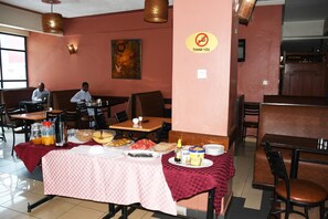 A restaurant with tables set for breakfast, including bread, fruit, and beverages. - Jamia Central Hotel (Nairobi)