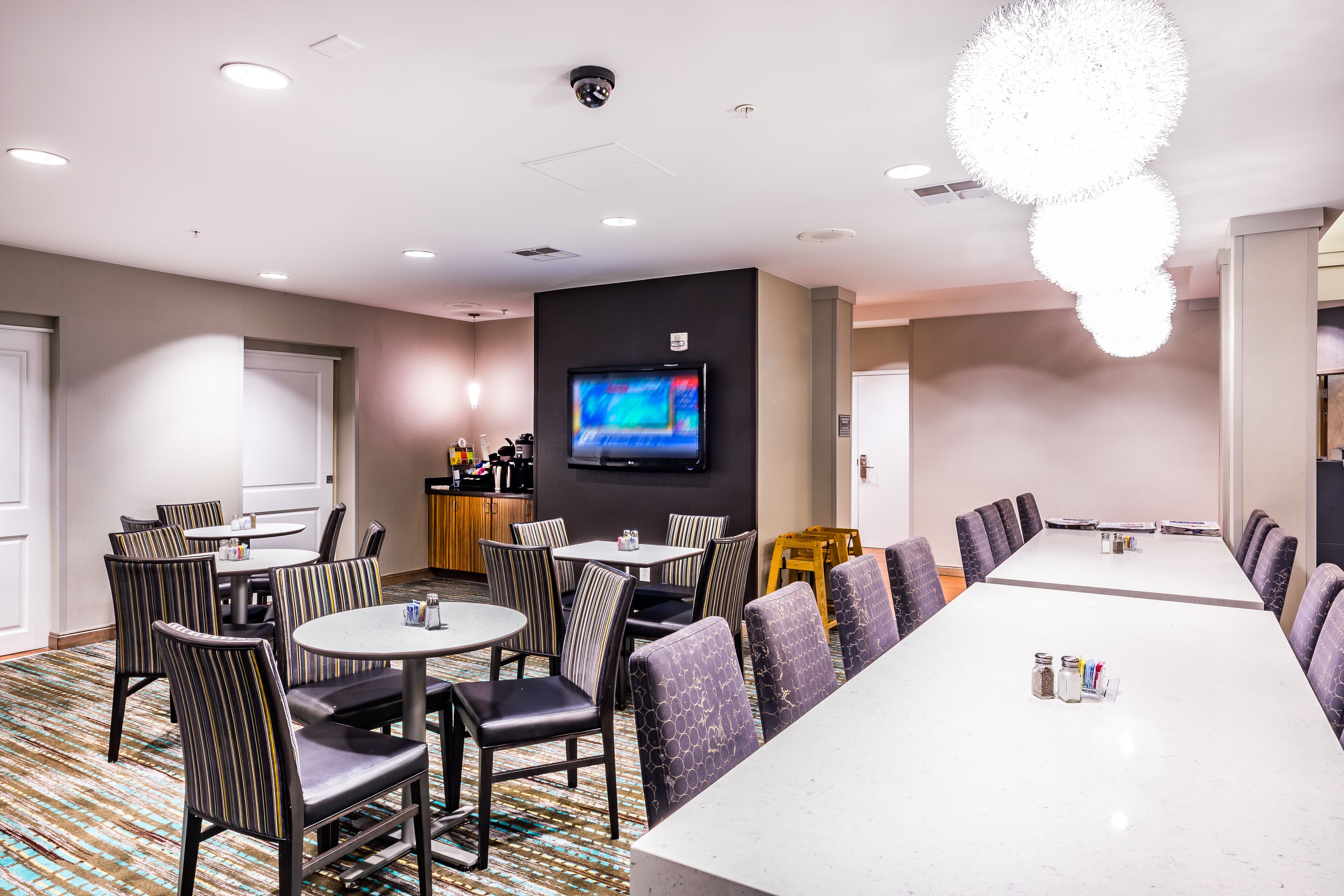 Uma sala de conferências de hotel com uma mesa comprida, mesas redondas e cadeiras.