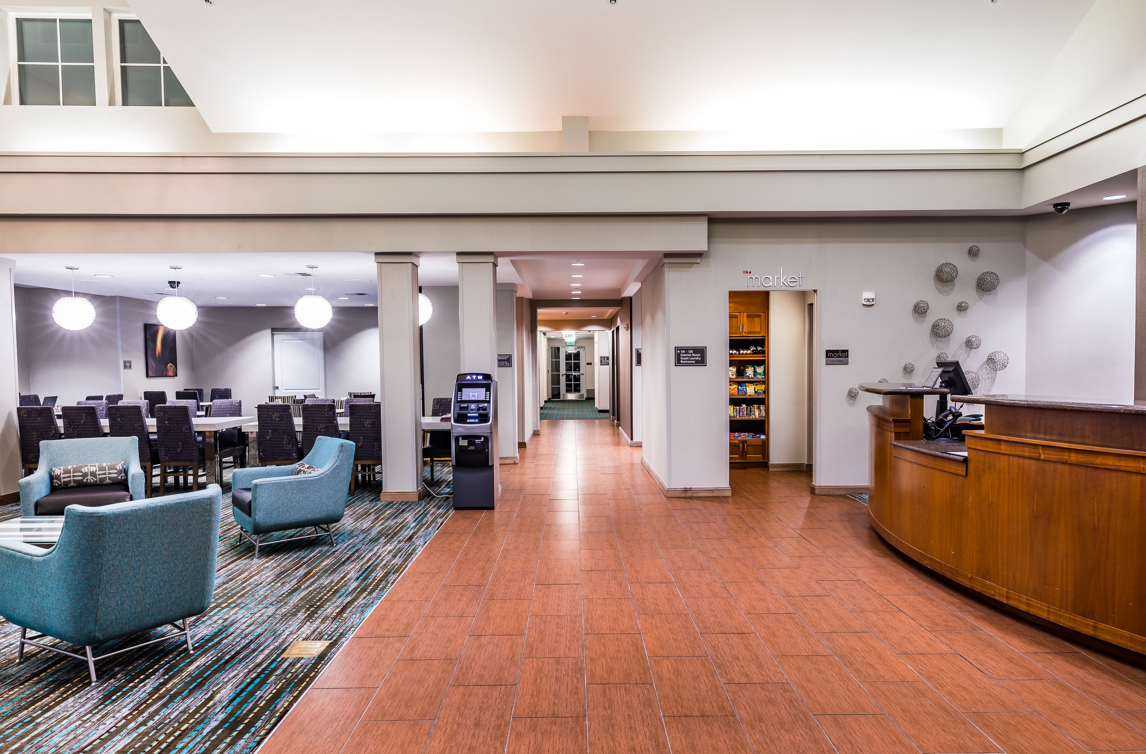 A hotel lobby with a reception desk, seating area, and a long corridor leading to other rooms.