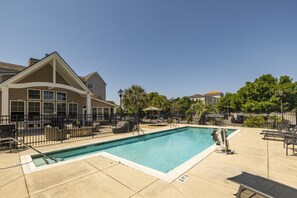 A swimming pool with a fenced area, lounge chairs, and a building with large windows in the background.