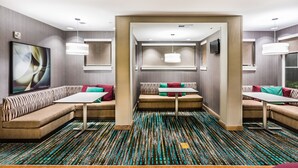 Un moderno vestíbulo de hotel con una zona de estar central, un gran cuadro abstracto y una alfombra estampada.