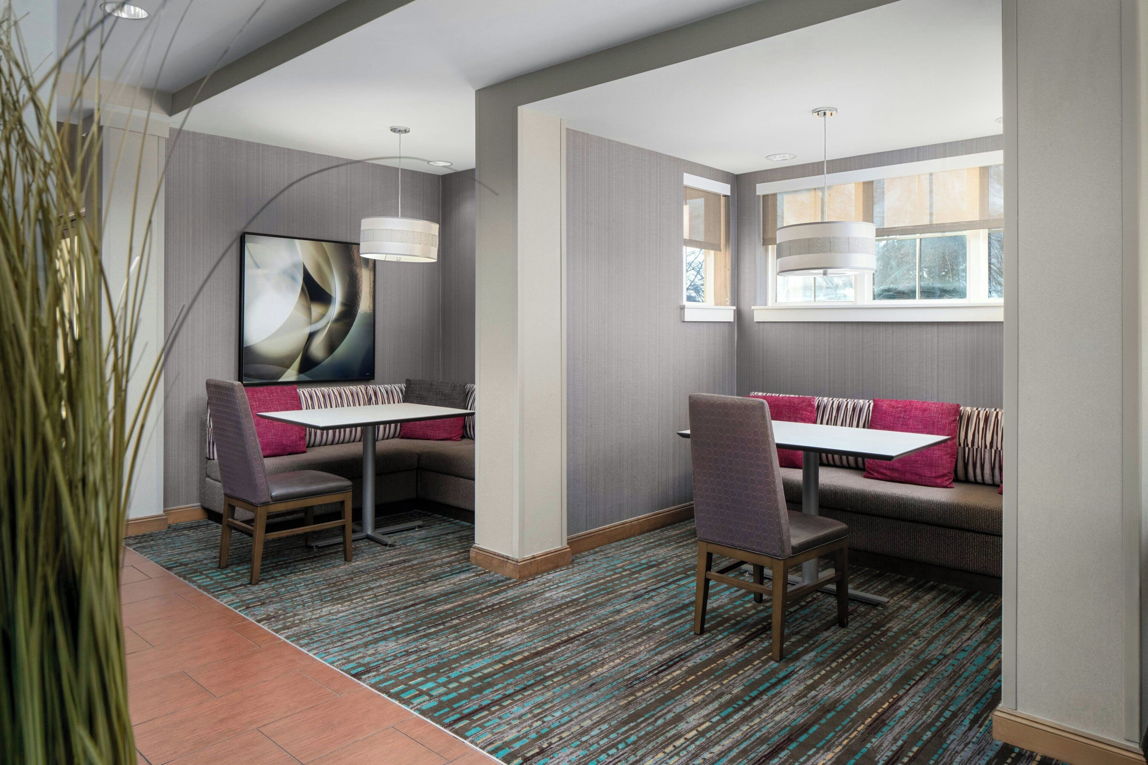A modern dining area with a high table and two chairs, a sofa with cushions, and a large abstract painting on the wall.