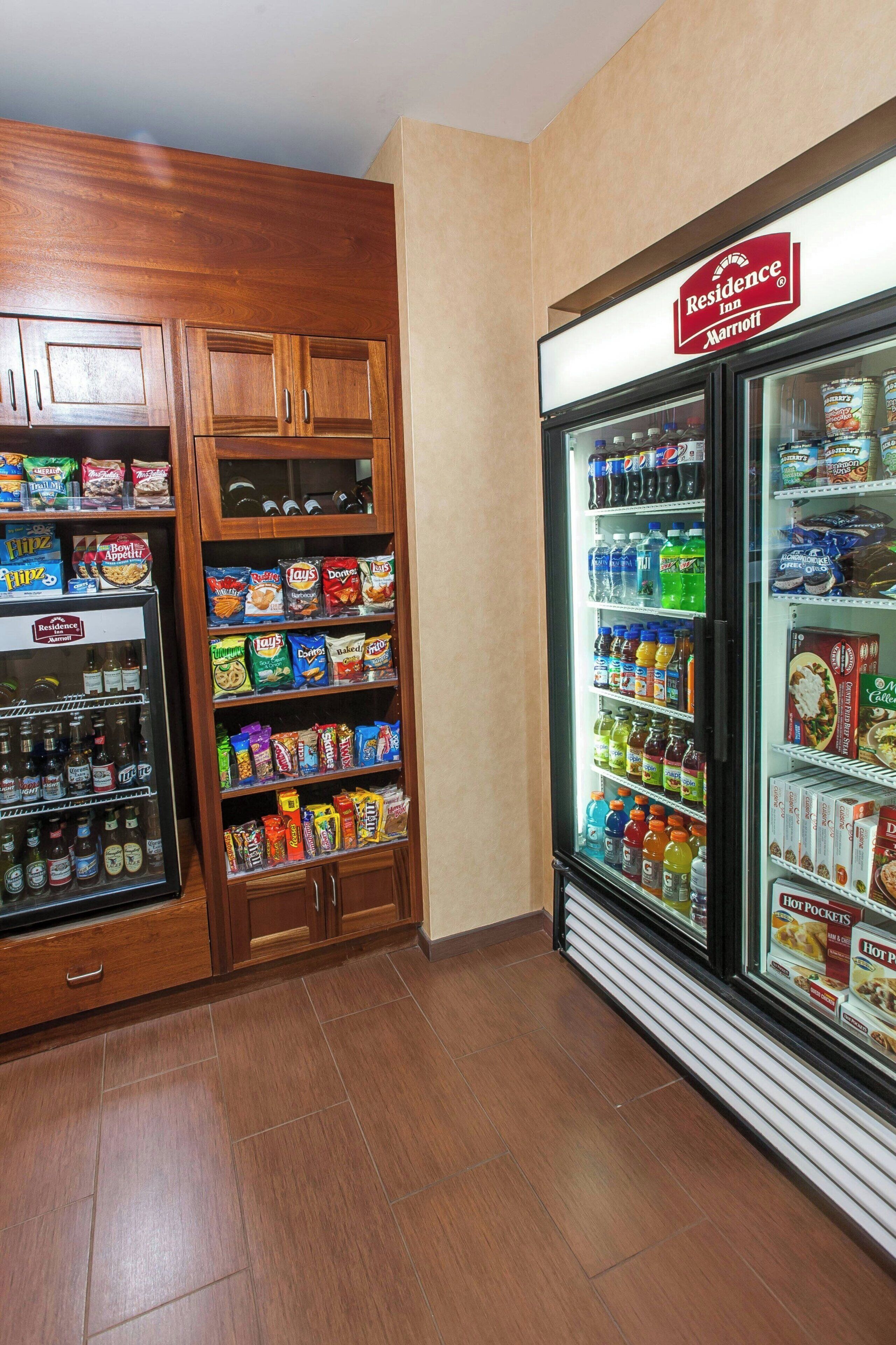 A hotel food service area with a refrigerated display case and a pantry stocked with snacks and beverages.