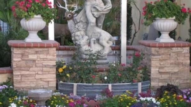 A garden with a stone statue of a woman and a deer, surrounded by various potted plants and flowers. - Palace Inn Oxnard (Oxnard)