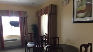 Un comedor con una mesa redonda y cuatro sillas, una planta en maceta y un amplio ventanal con cortinas.