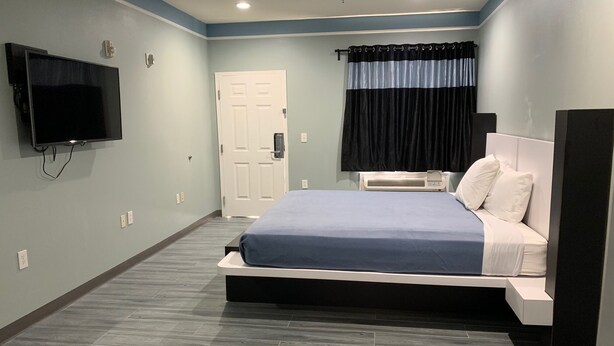 Un dormitorio moderno con cama, televisión montada en la pared, una puerta y equipo de aire acondicionado.