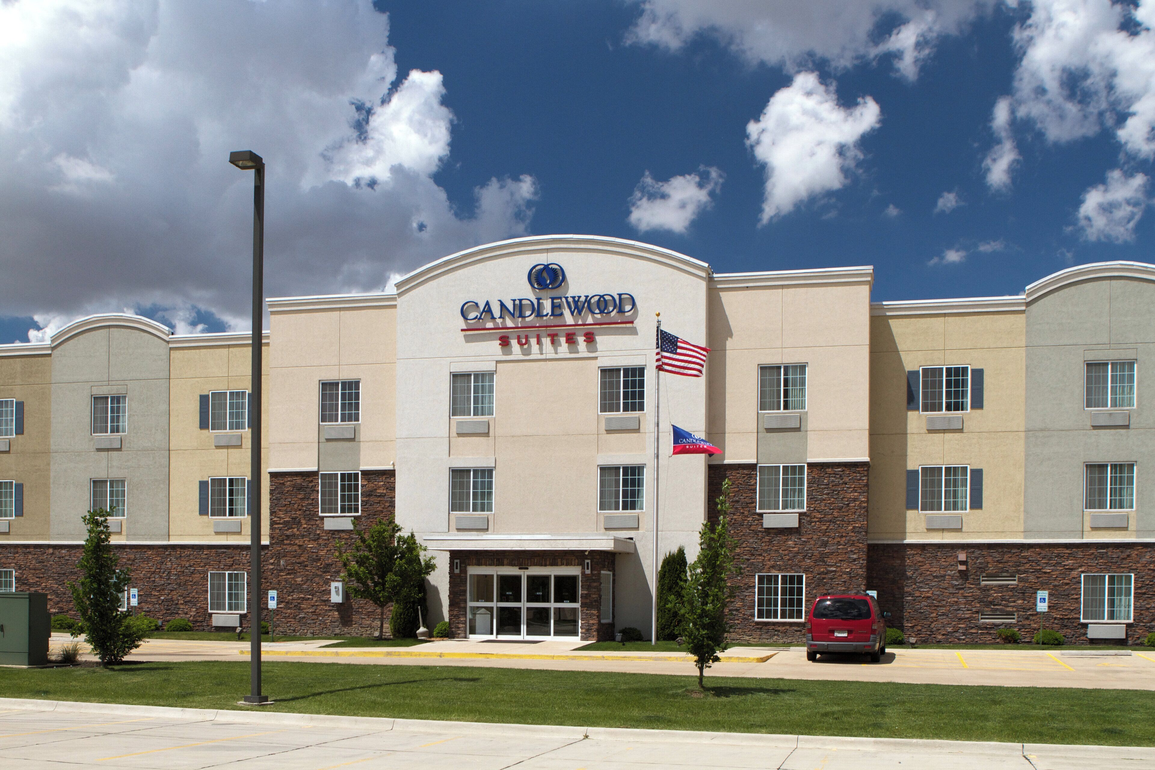 Ein Hotel mit einem gut sichtbaren 'CANDLEWOOD SUITES' Schild, mehreren Fenstern und einem Parkplatz.