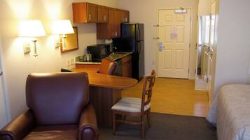 A compact hotel room with a kitchenette, a dining area with a table and chairs, a bed, and a door.