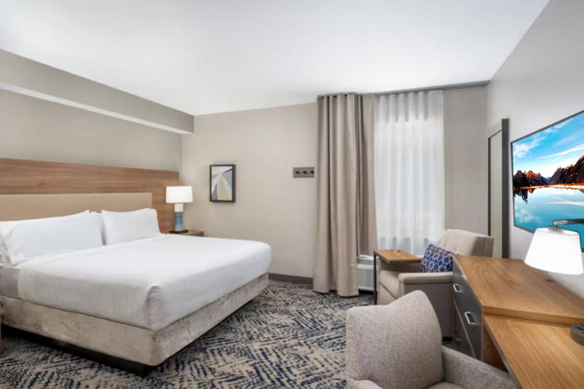 Een hotelkamer met een groot bed, een bureau met stoel, een televisie en een raam met gordijnen.