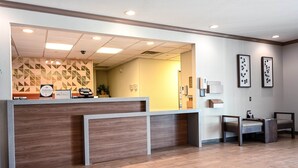 A reception area with a wooden reception desk, a waiting area with two chairs, and a patterned wall in the background.