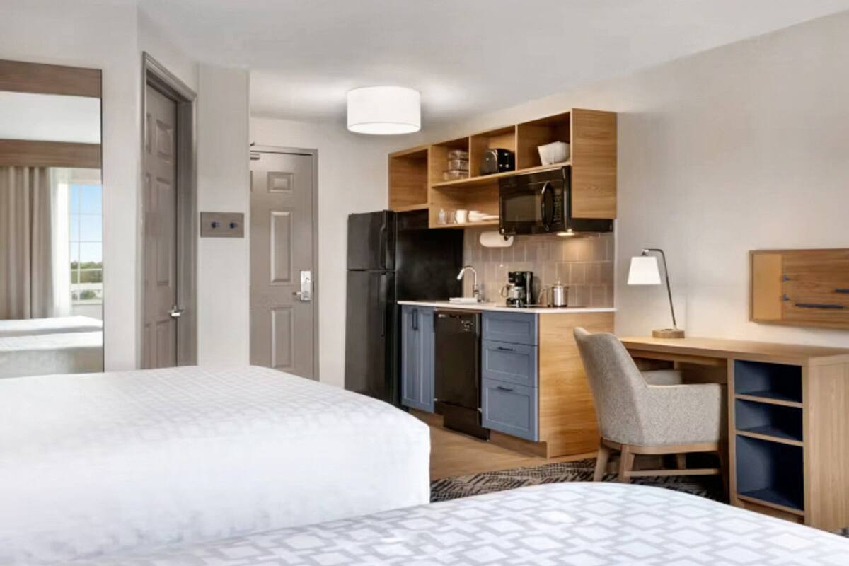 Een hotelkamer met een bed, een bureau met stoel, een kitchenette en een deur.