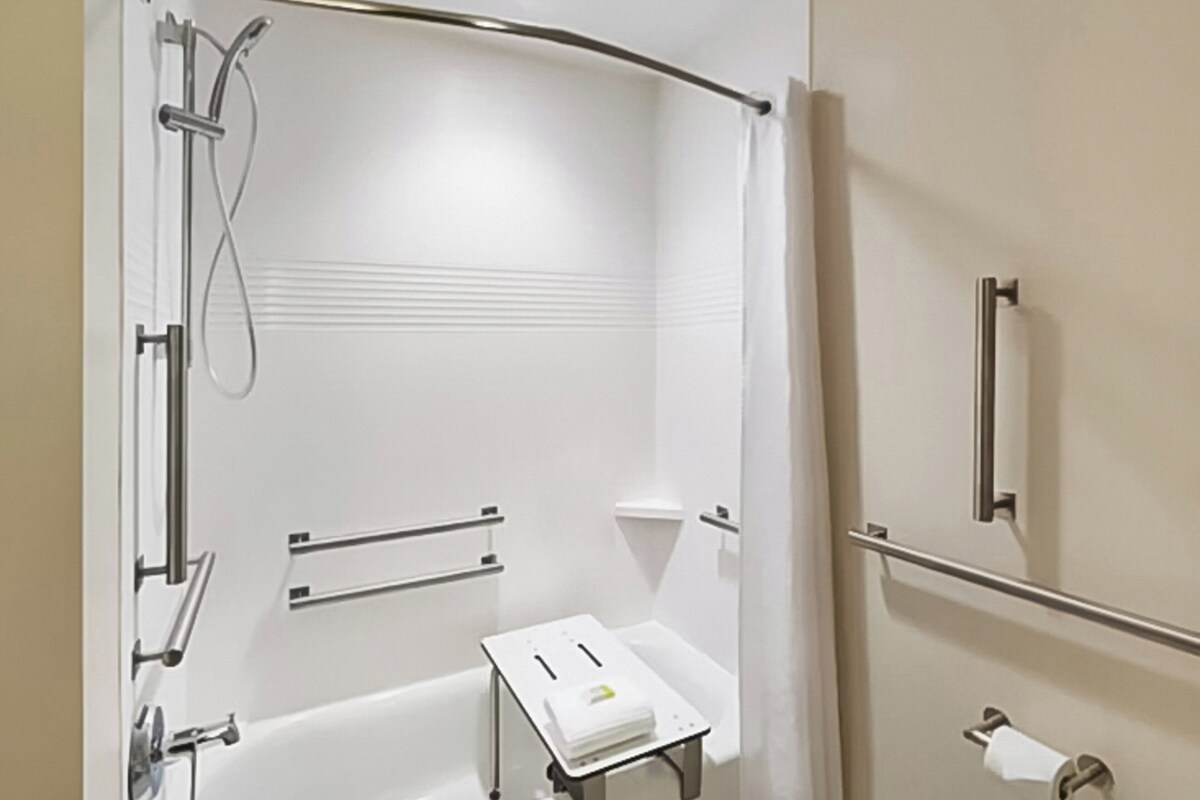 Une salle de bain moderne dotée d’une douche à l’italienne, de barres d’appui, d’un porte-serviettes et d’un support à papier toilette.