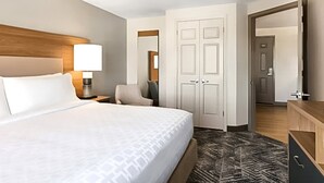 Habitación de hotel con cama, mesita de noche, silla, armario y puerta que da a otra habitación.