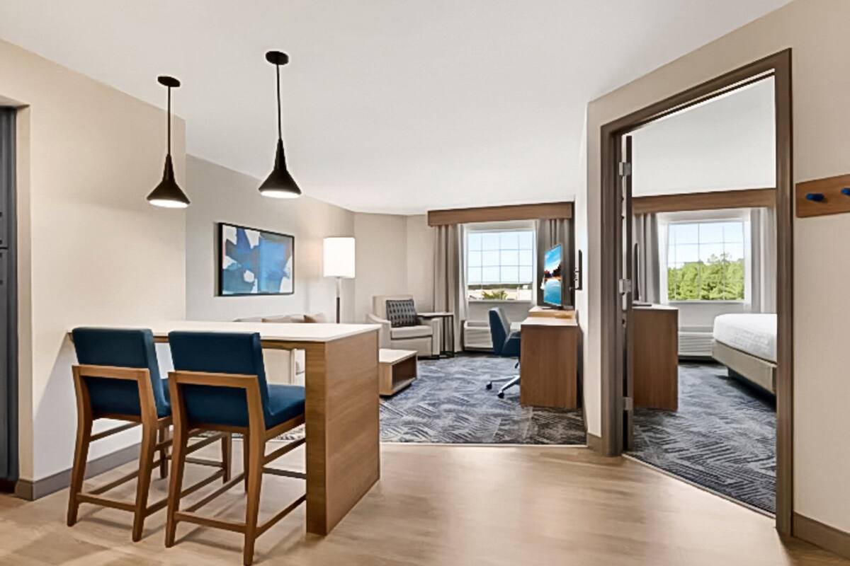 Hotelkamer met een bureau, twee stoelen, een bed, een televisie en een raam met uitzicht op bomen.