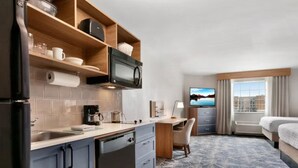 A compact hotel room with a kitchenette, a bed, a desk, and a TV.