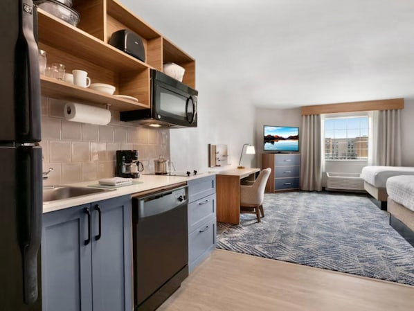 A compact hotel room with a kitchenette, a bed, a desk, and a TV.