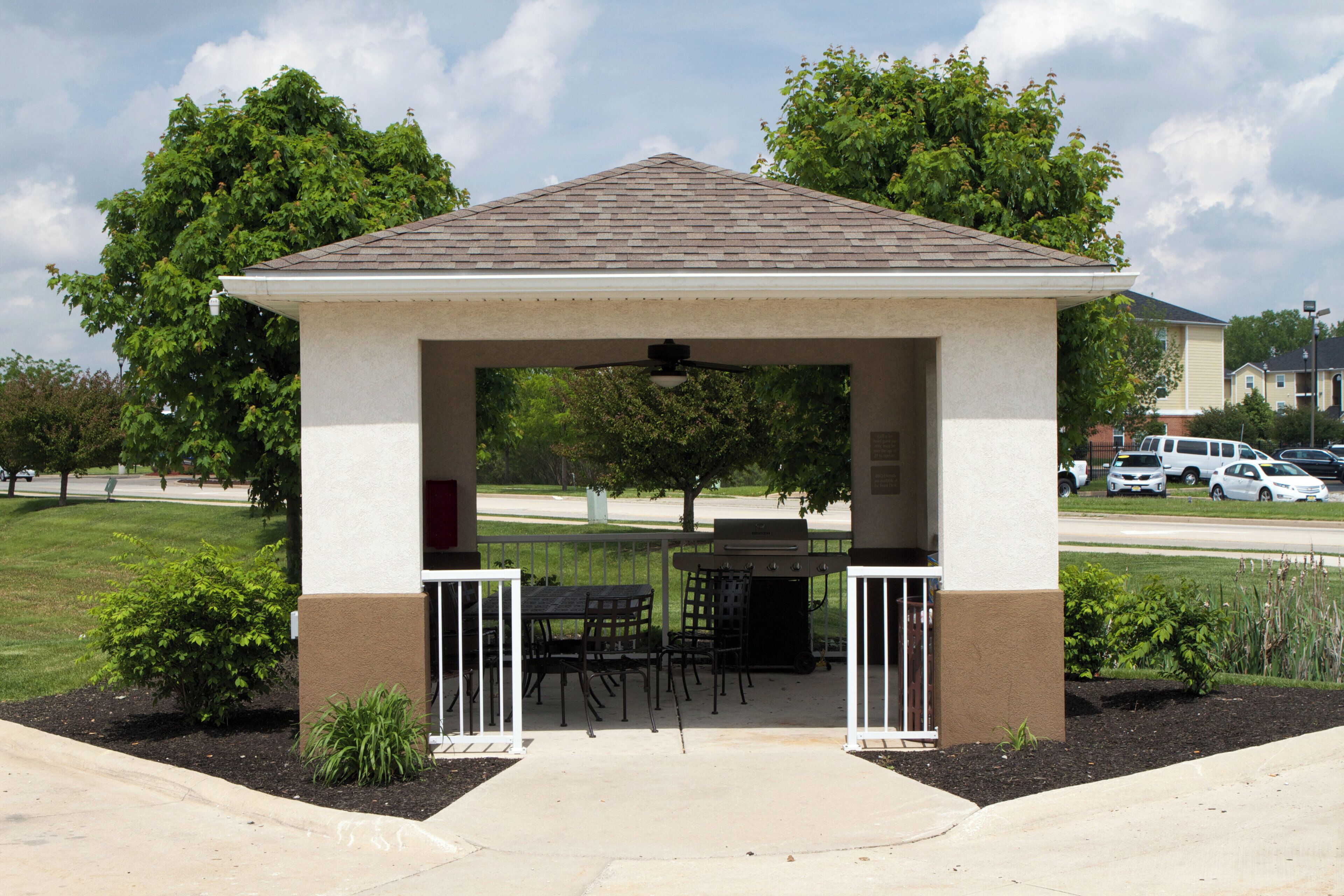 A covered outdoor seating area with a table and chairs, surrounded by a landscaped garden.